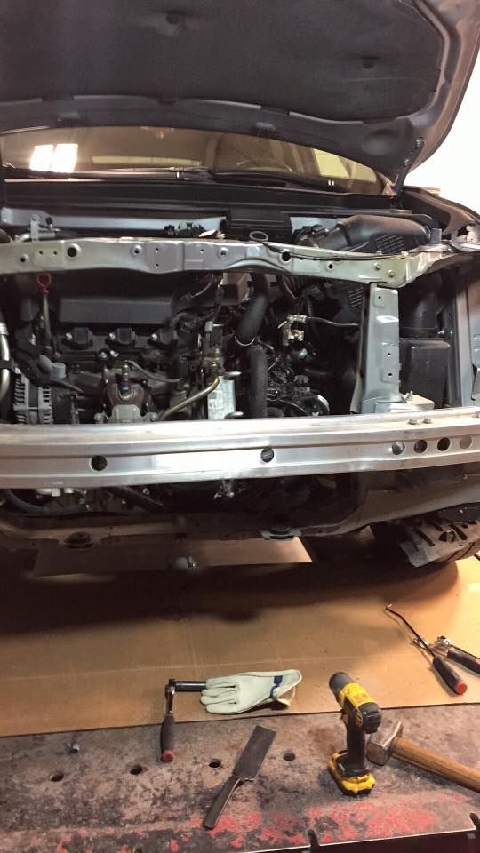 Car engine bay with open hood. Tools on a table below.
