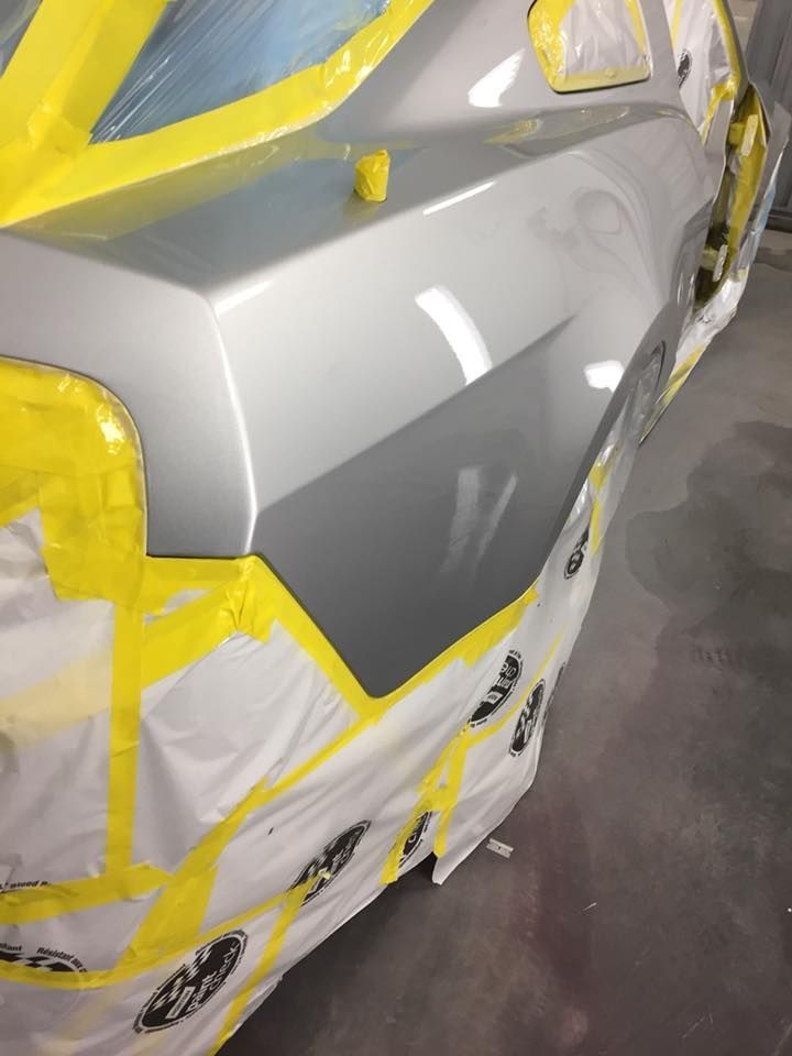 Car panel, silver paint, taped off for painting, shop setting.