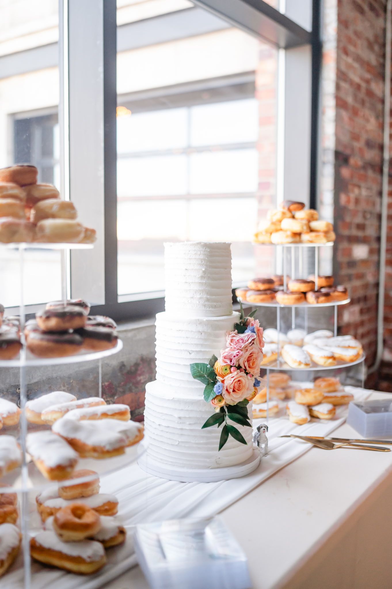 A wedding cake is sitting on top of a table surrounded by donuts.
