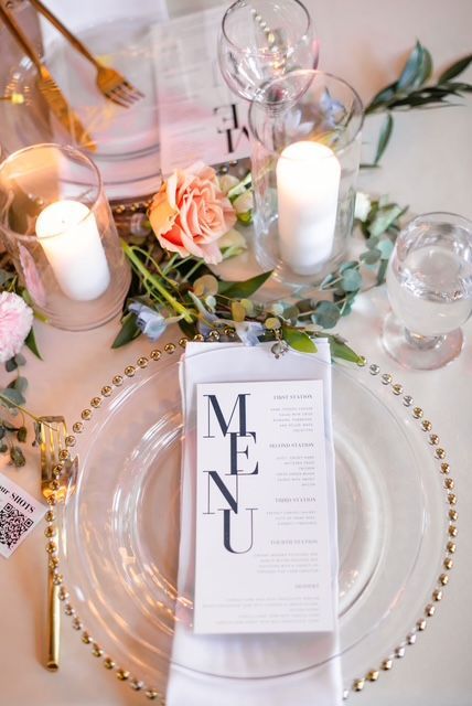 A menu is sitting on a plate on a table with candles and flowers.