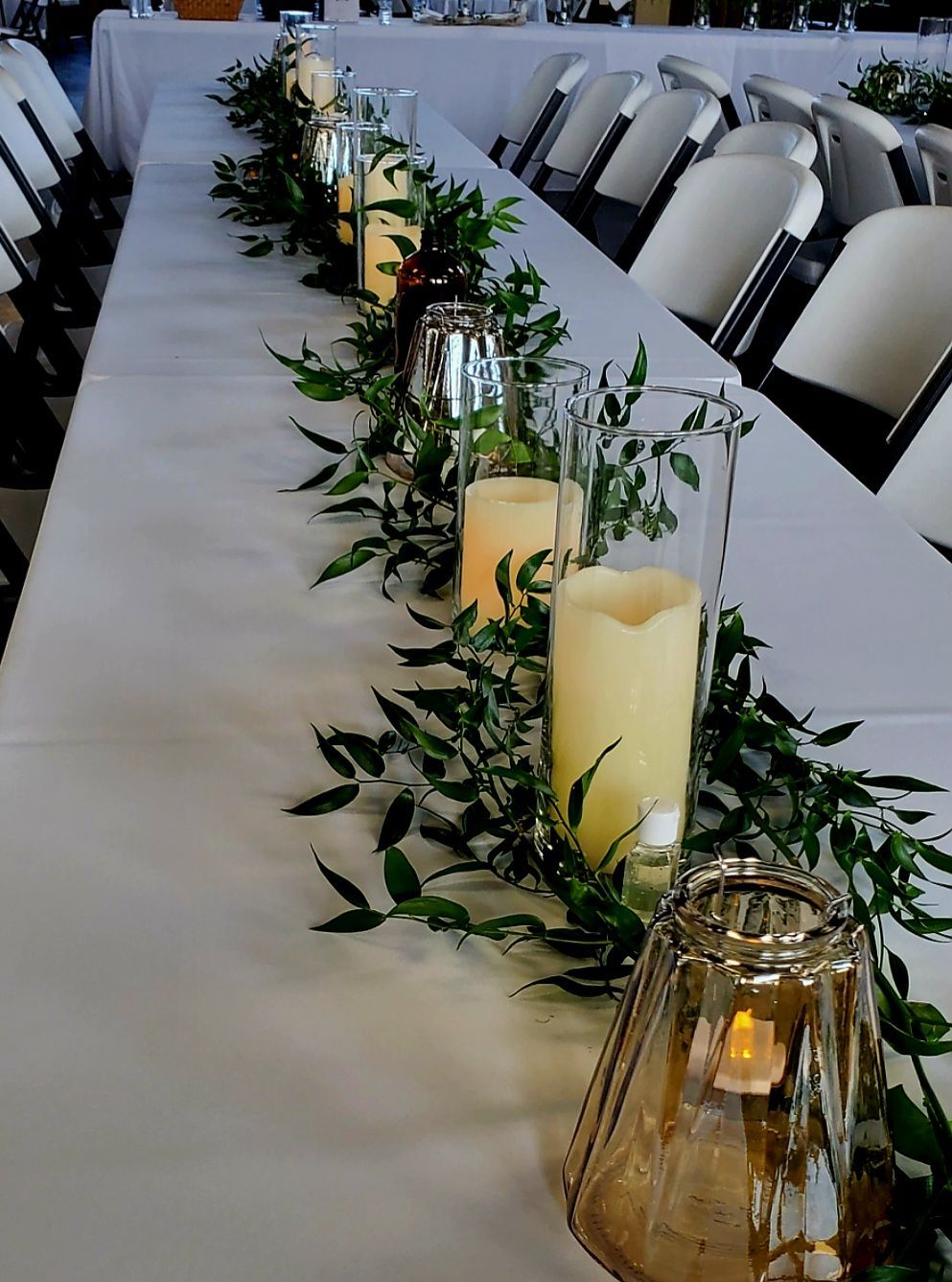 A long table with candles and greenery on it.