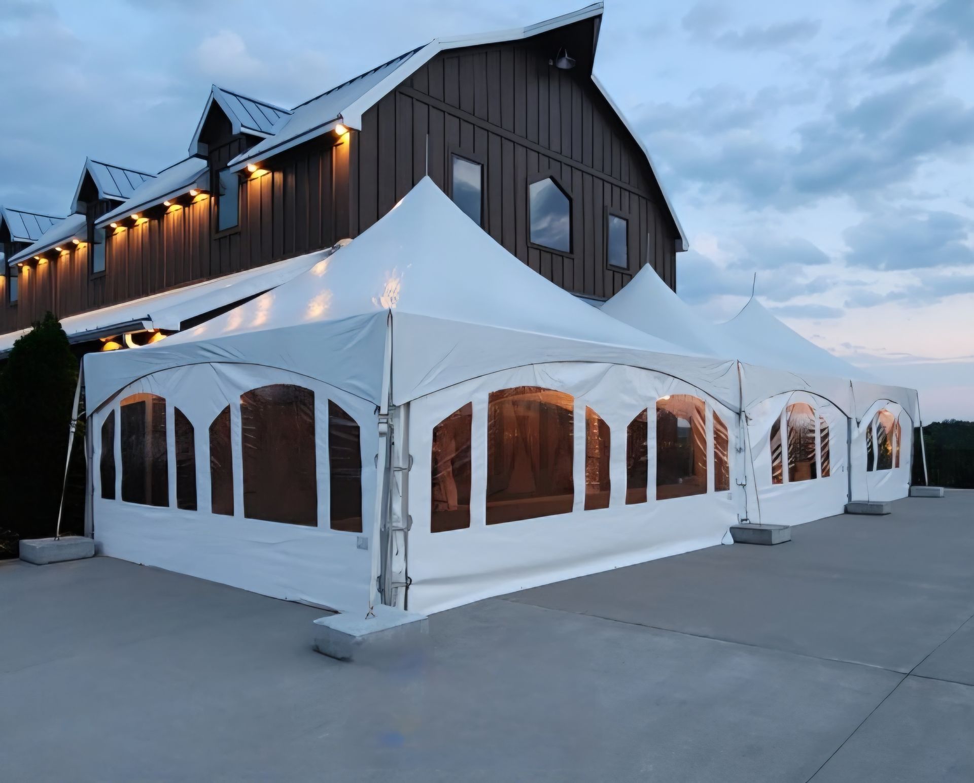 A large white tent is sitting in front of a barn.