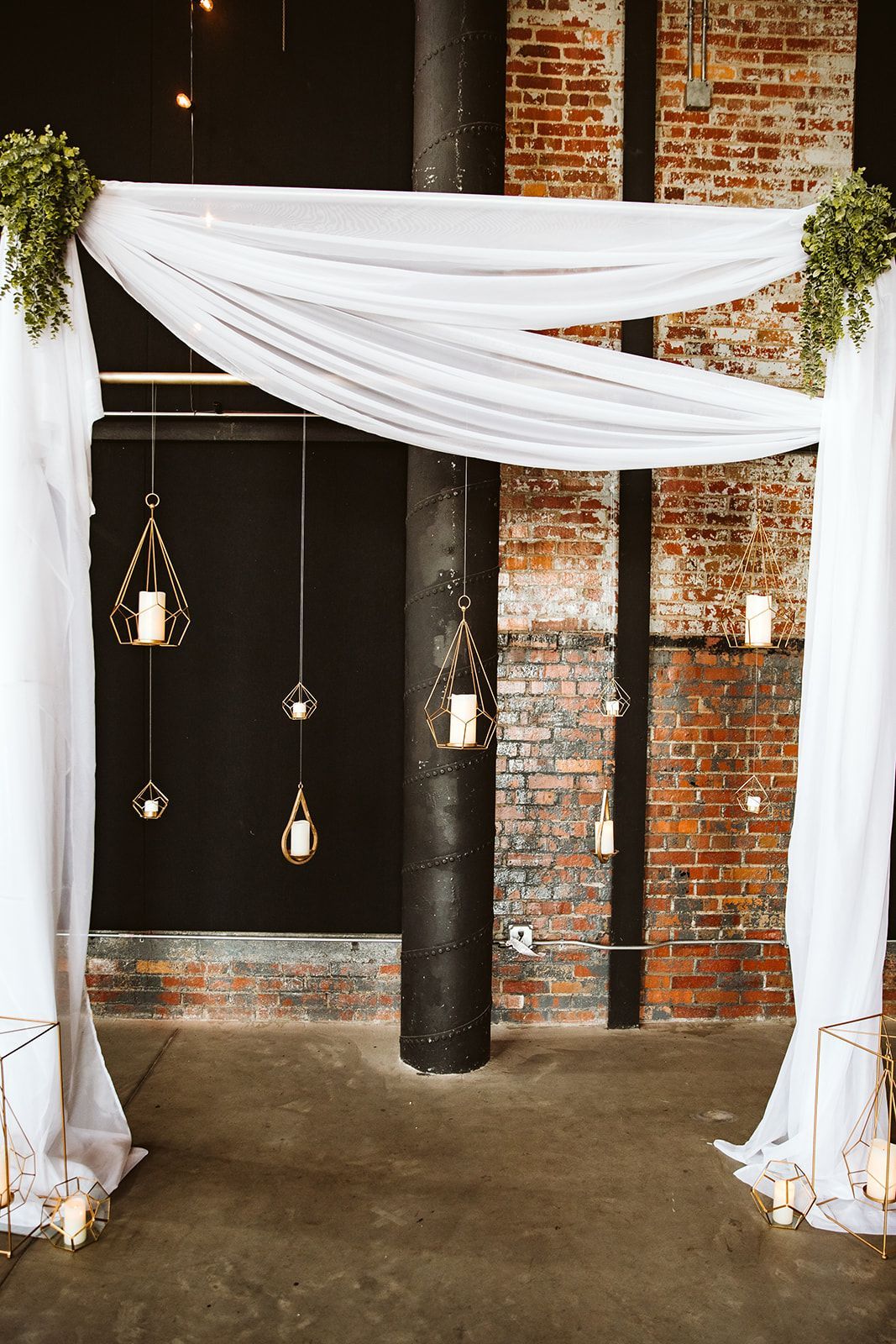 A white arch with candles hanging from it in front of a brick wall.