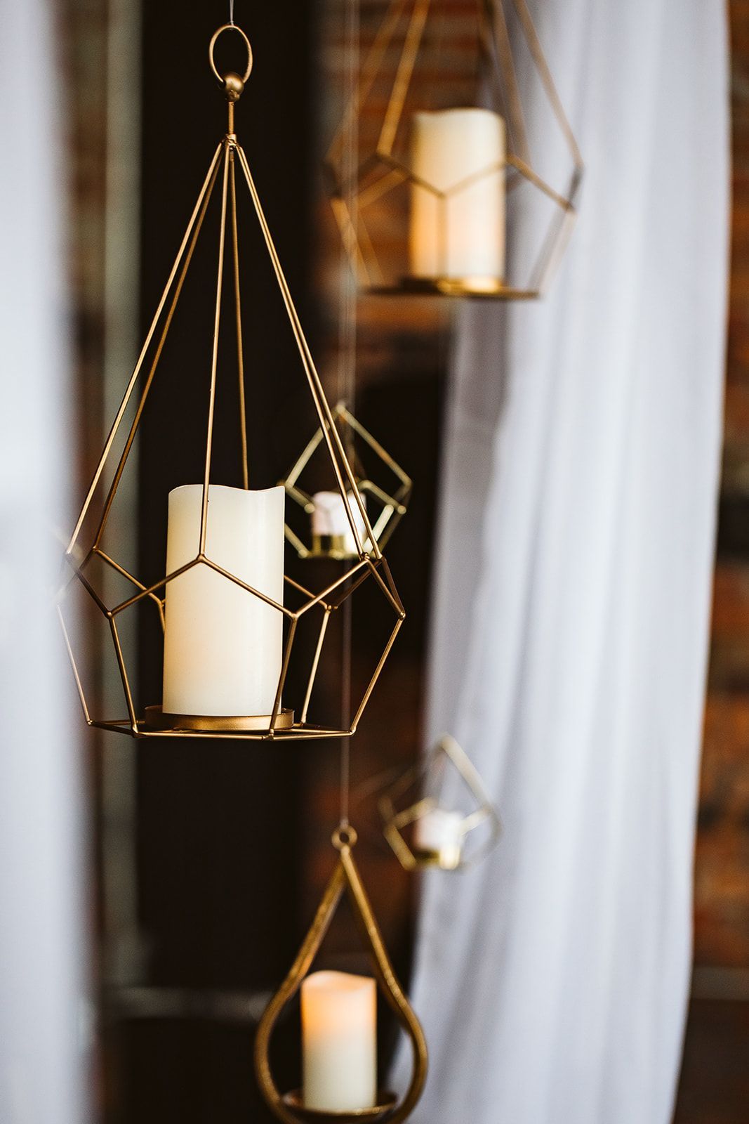 A row of candles hanging from a ceiling in geometric candle holders.