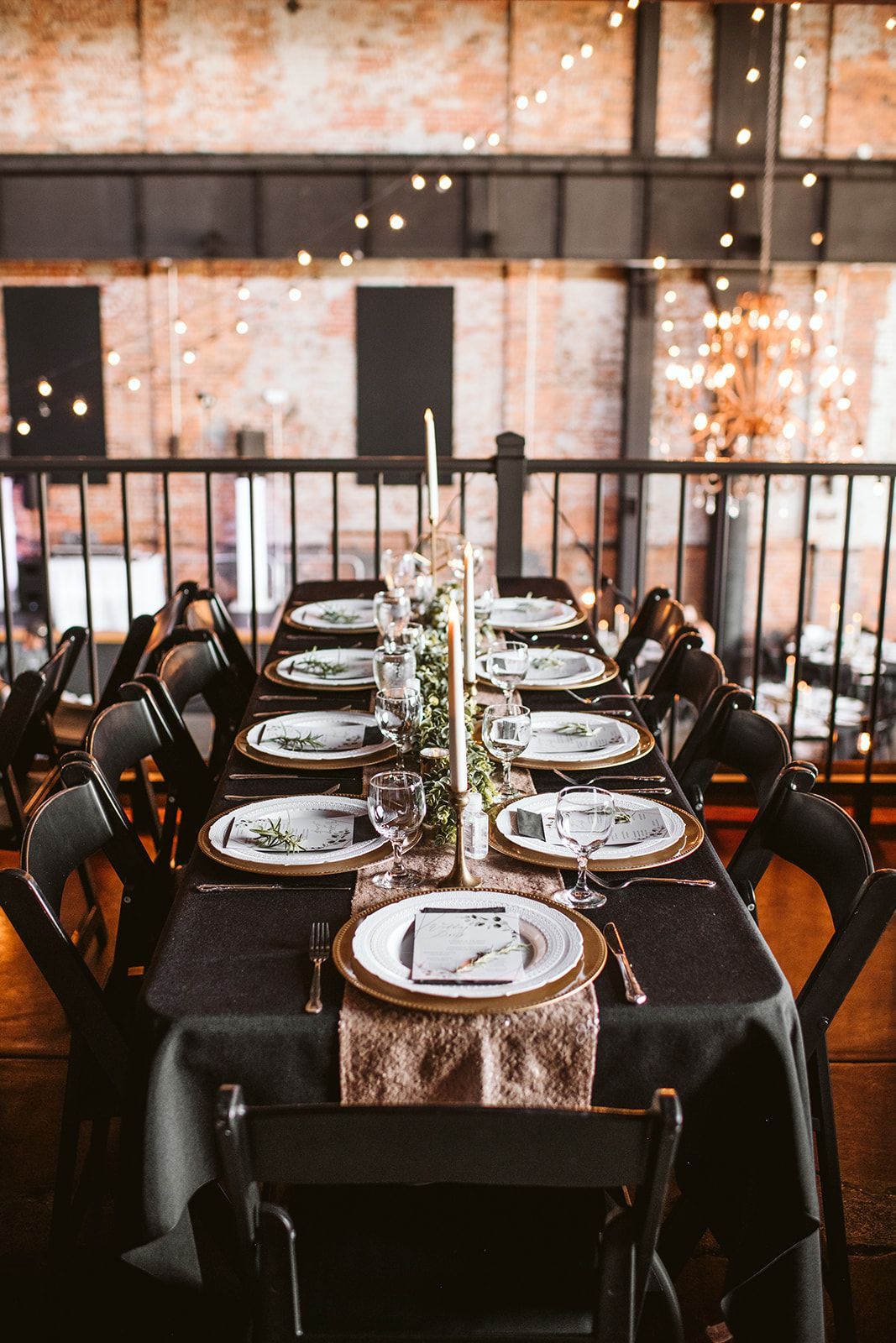 A long table with plates , candles , and chairs set for a wedding reception.