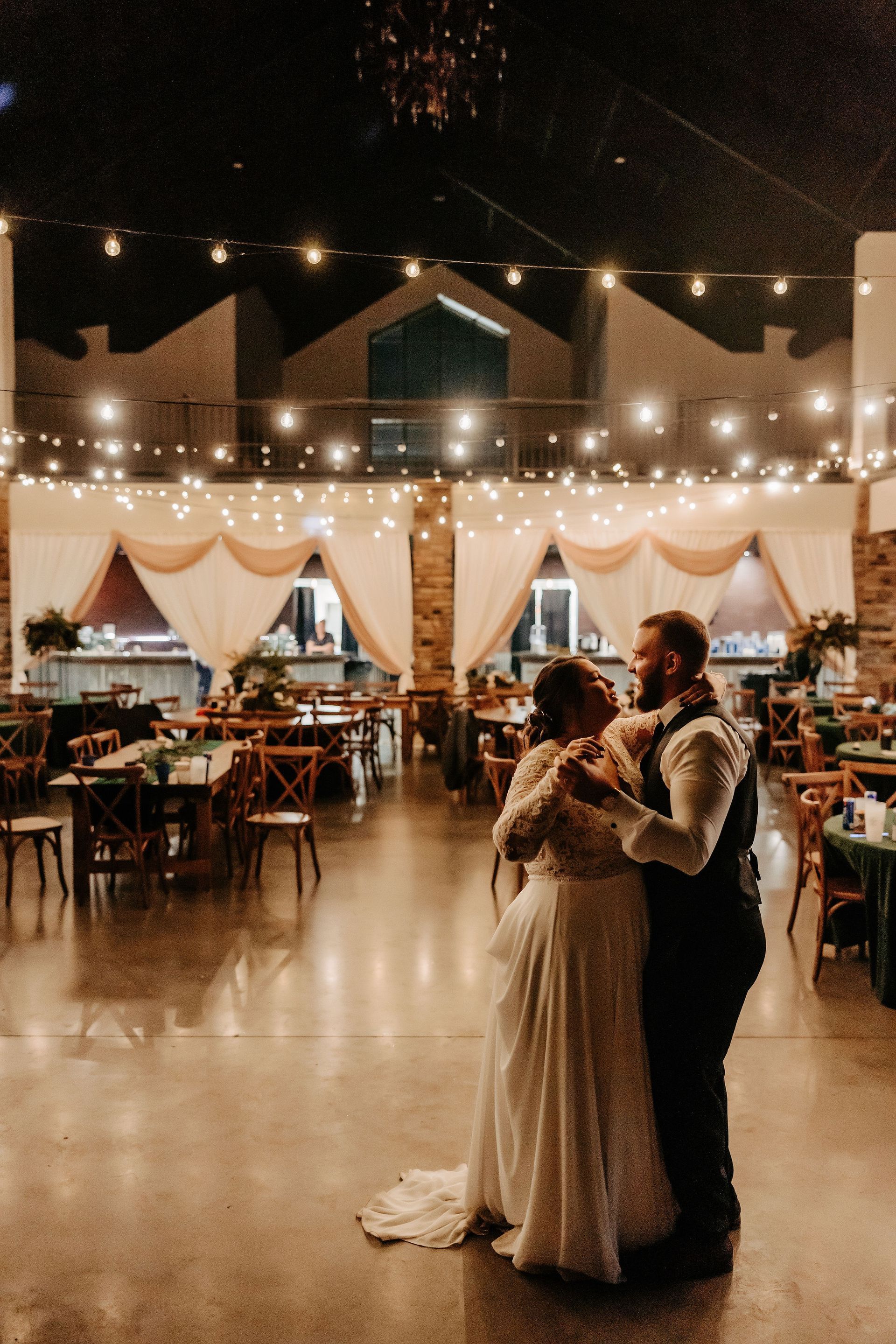 A bride and groom are dancing in a large room at their wedding reception.