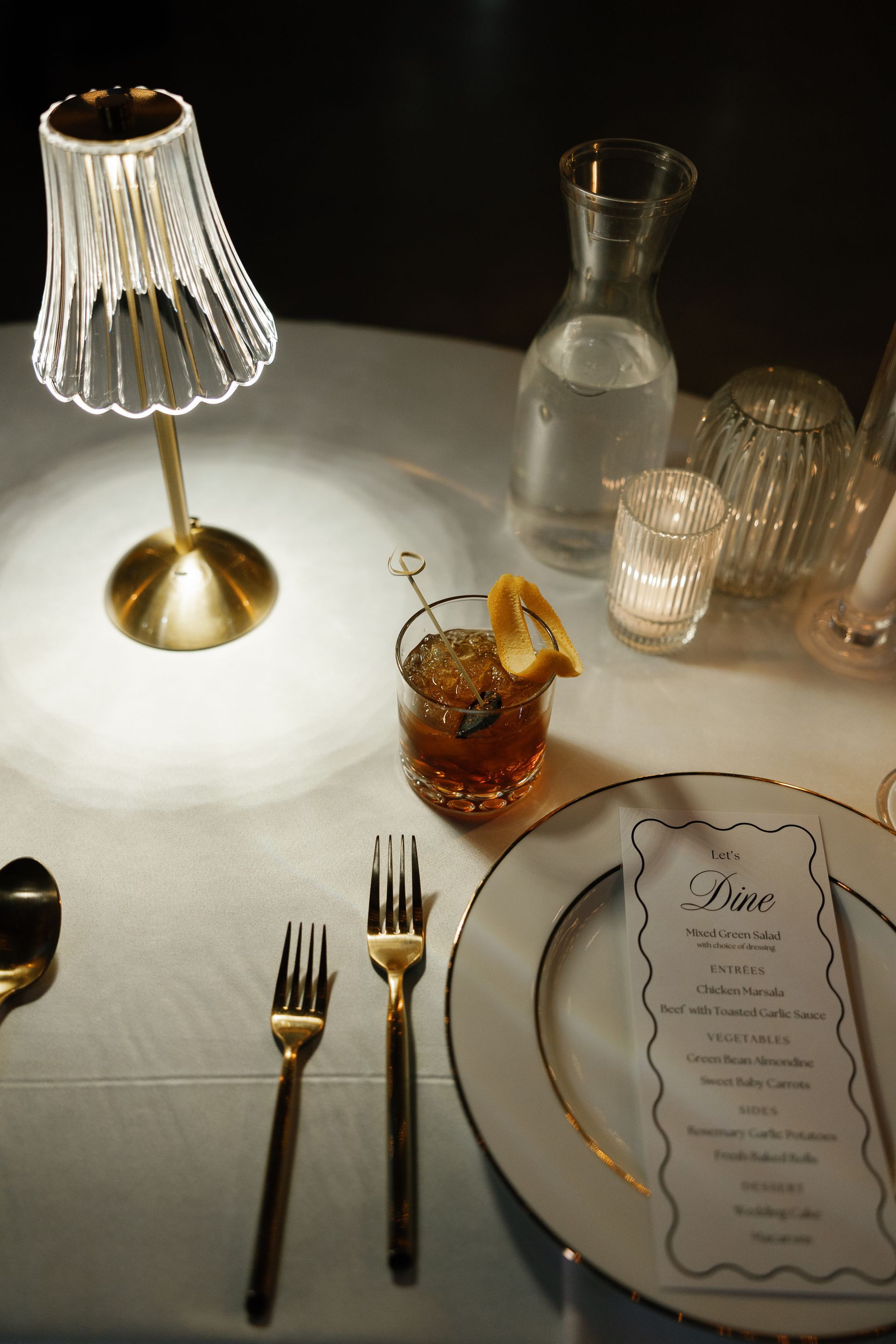 A table with plates , forks , spoons , a lamp and a menu.