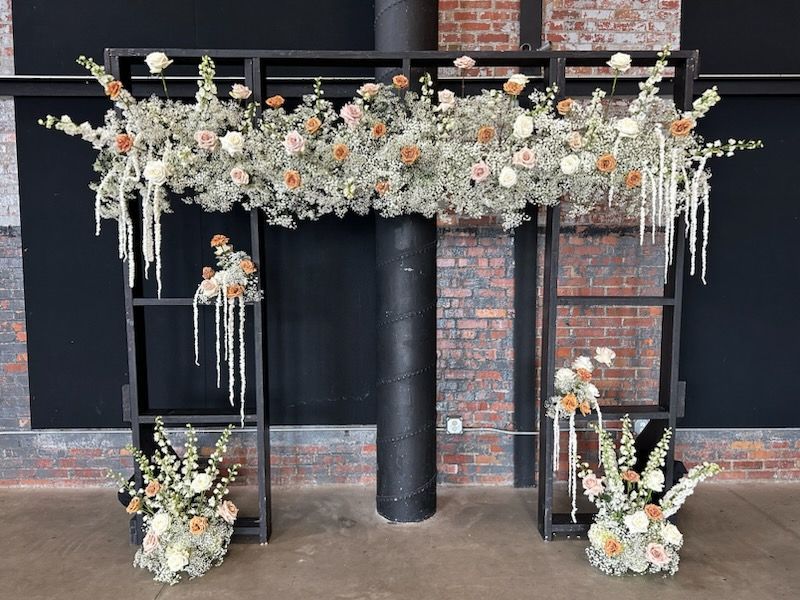 A black arch with flowers on it is in front of a brick wall.