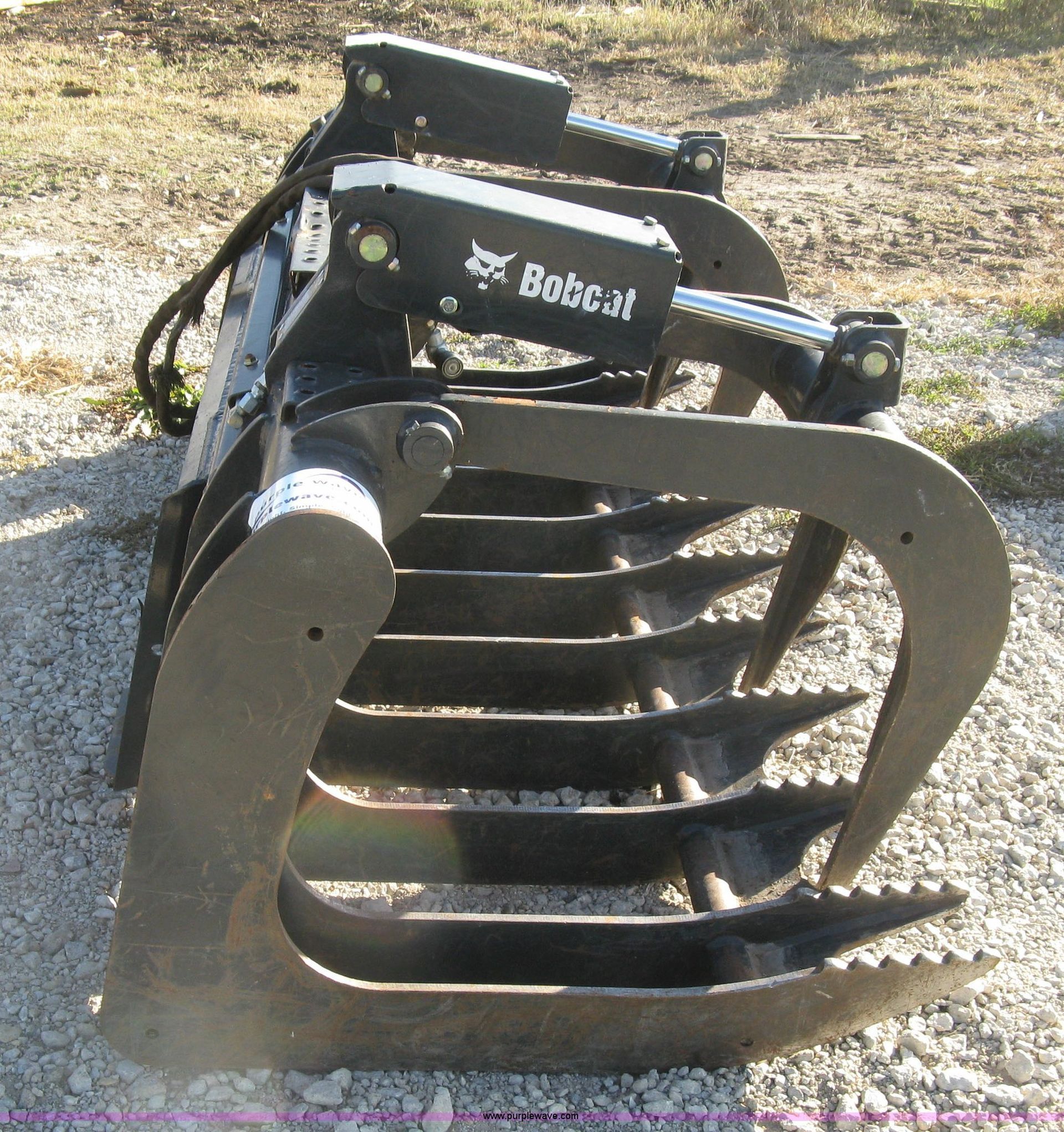 A bobcat grapple is sitting on a gravel road