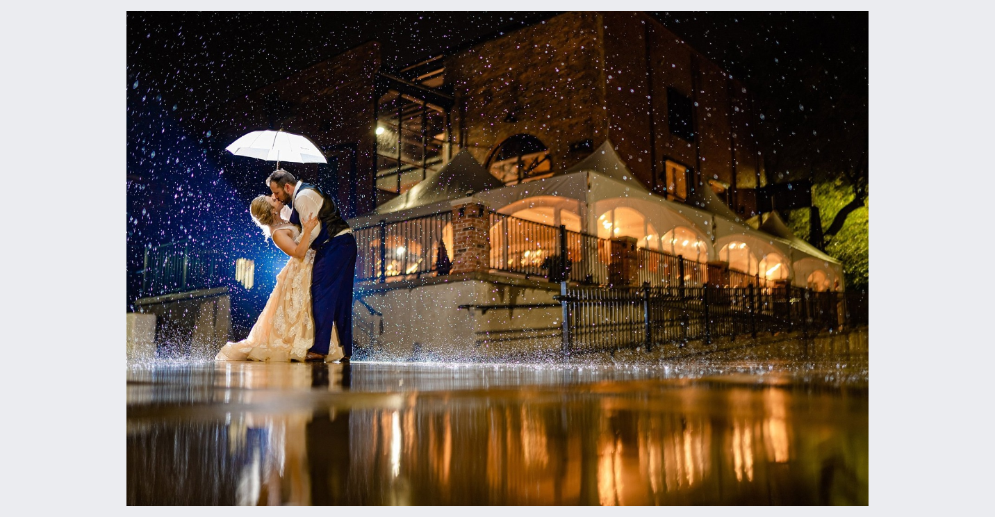 A bride and groom are kissing under an umbrella in the rain.