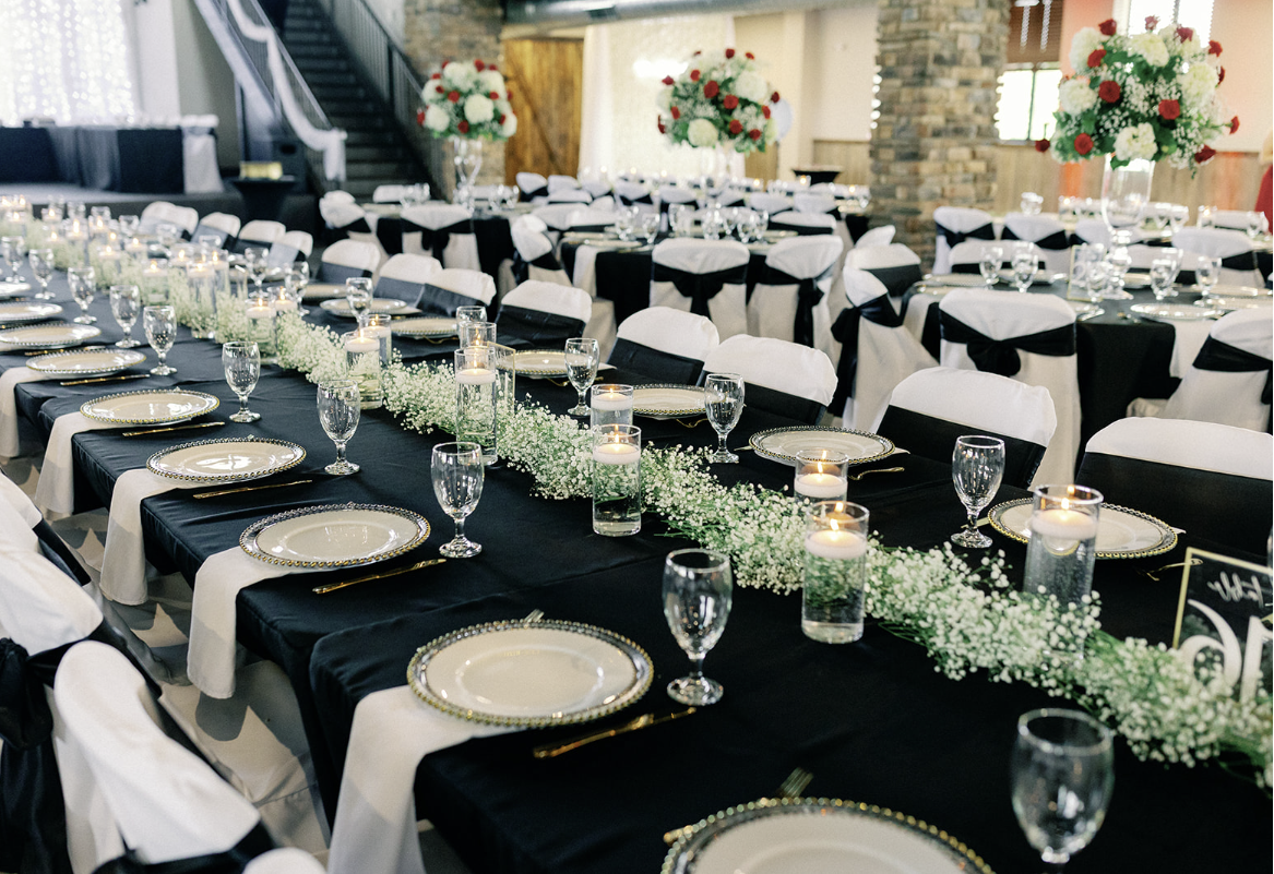 A long table set for a wedding reception with black tables and white chairs.