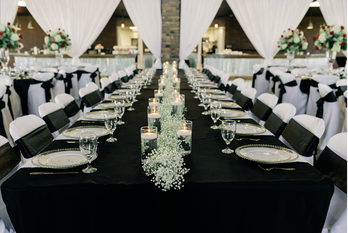 A long table with plates , glasses , candles and baby 's breath on it.