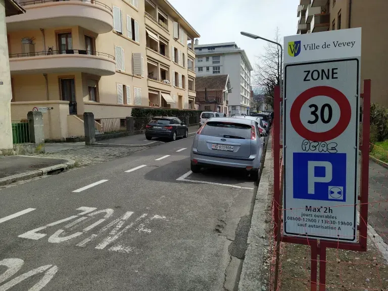 Des cyclistes circulent sur une piste cyclable devant un ancien bâtiment industriel couvert de graffitis.