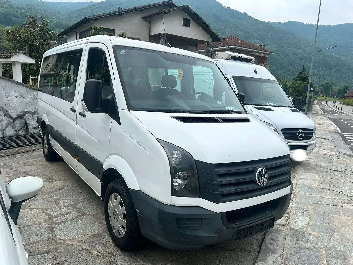 Due furgoni bianchi parcheggiati su una strada di montagna bagnata accanto a una casa