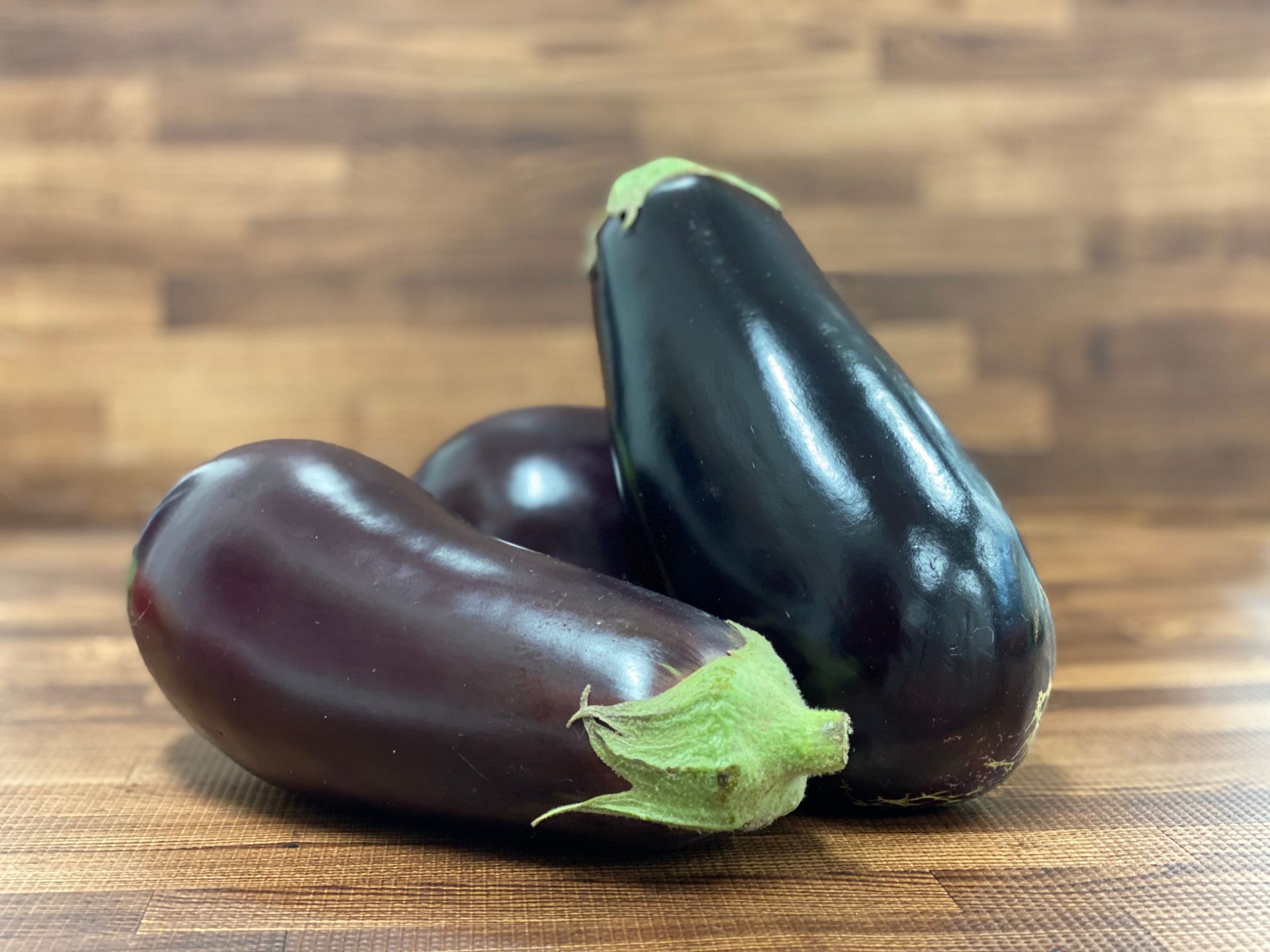 Three eggplants, varying shades of purple, on a wooden surface.