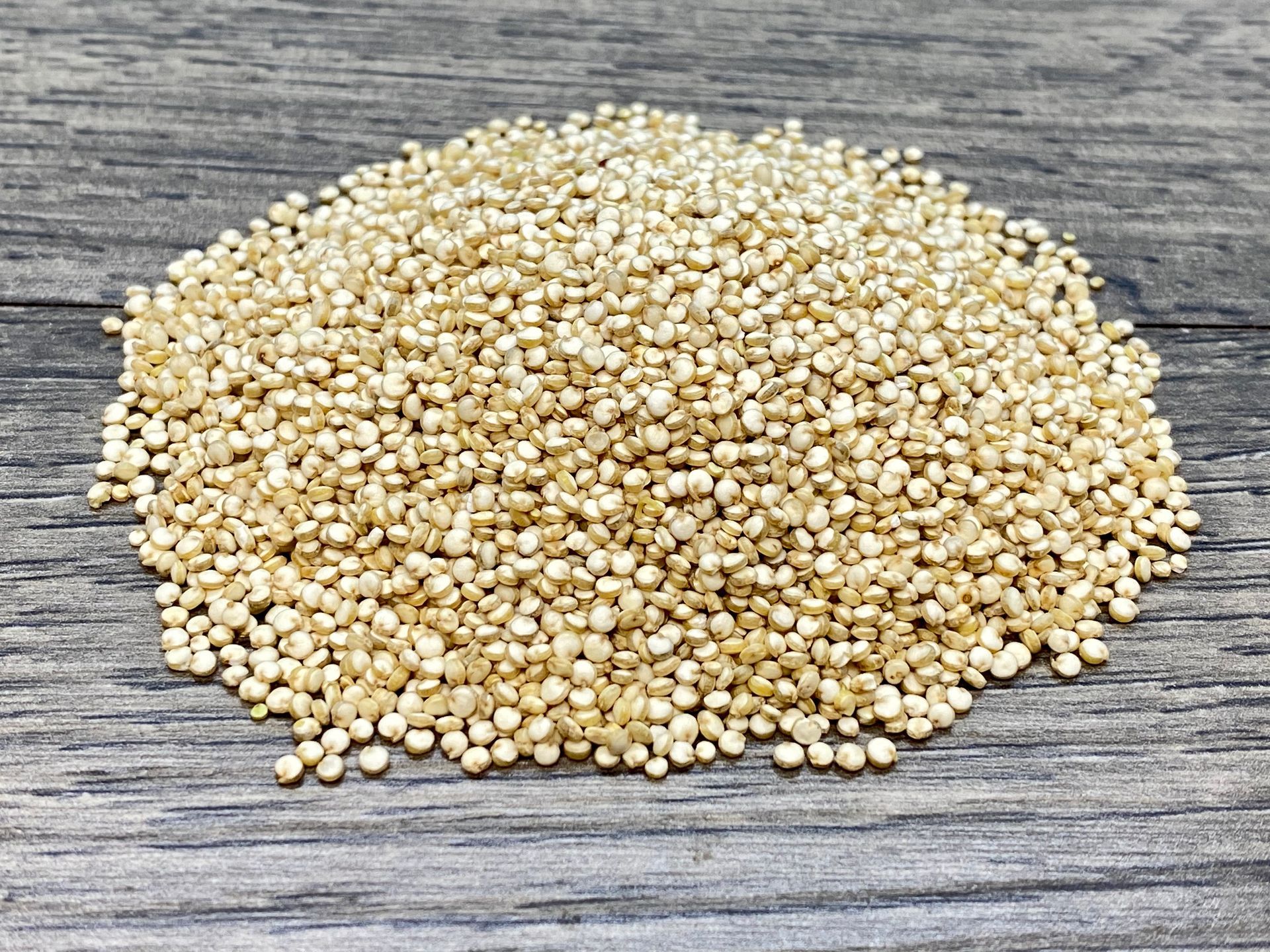 Pile of white quinoa seeds on a weathered wooden surface.