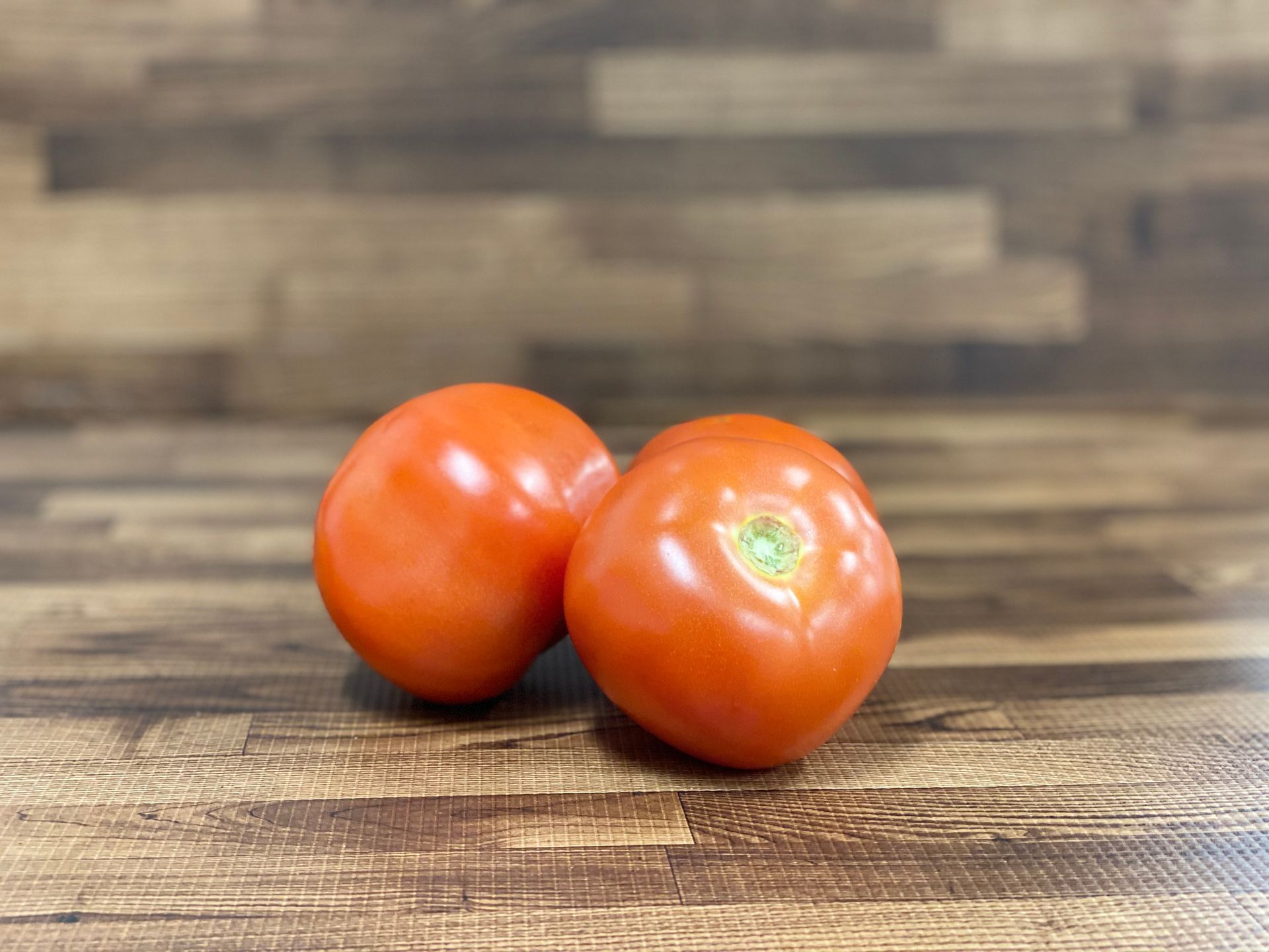 Two red tomatoes on a wooden surface, likely for cooking or eating.