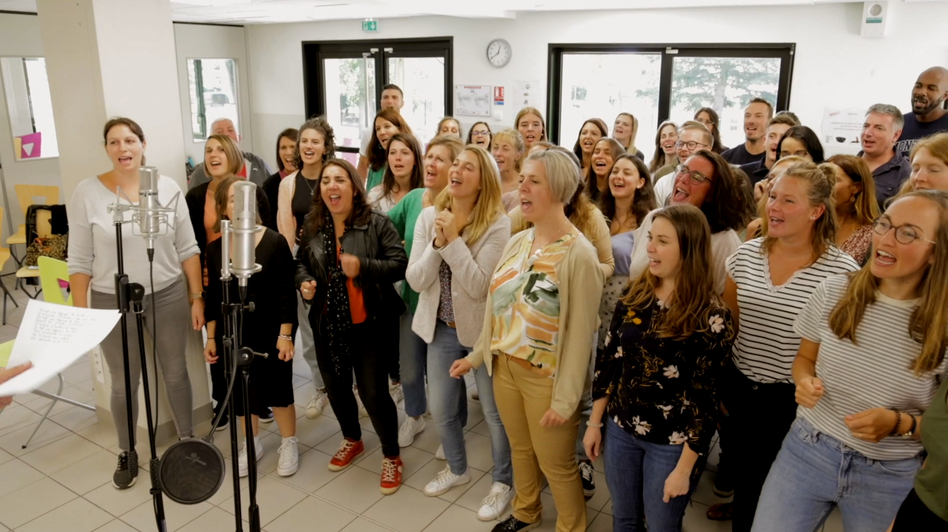 Un grand groupe de personnes chantent dans des microphones dans une pièce.