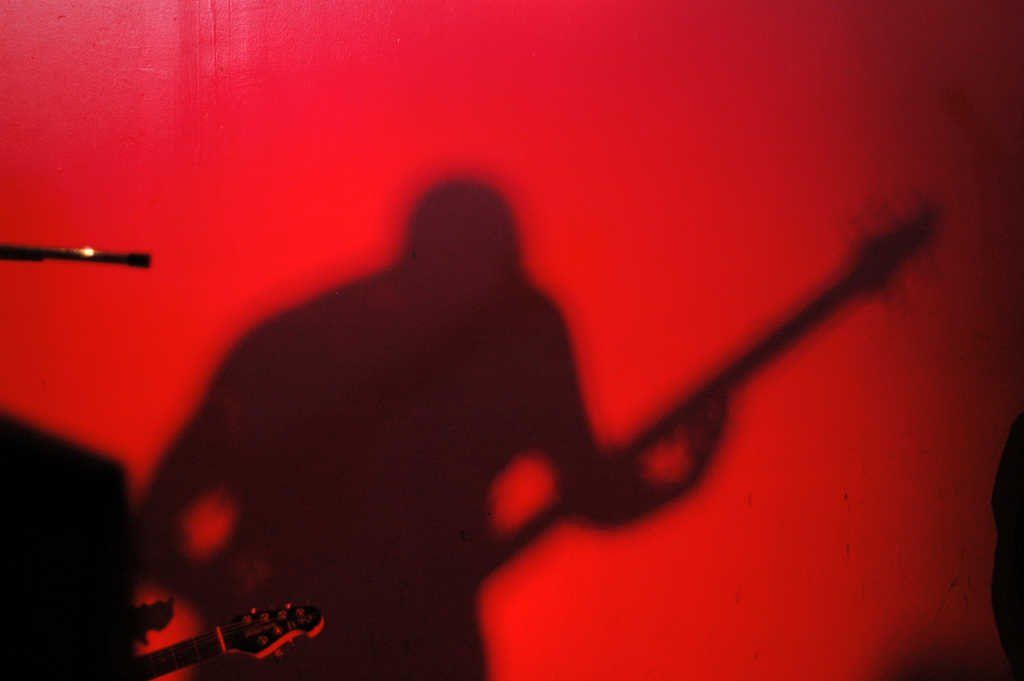 Une ombre d'une personne jouant de la guitare sur un fond rouge.