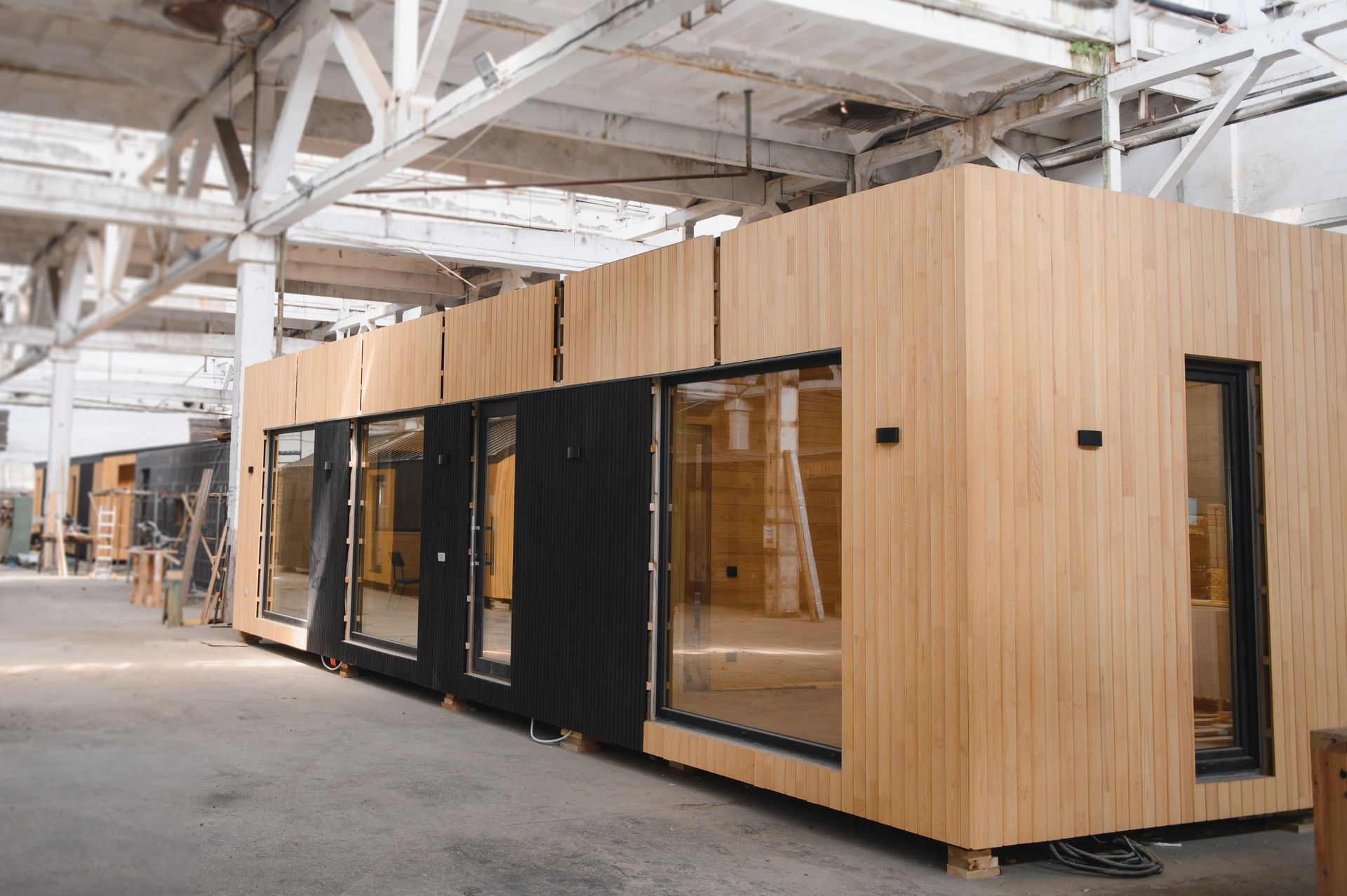 Modular wooden building in a warehouse, with black-framed windows and doors.