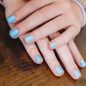 Hands with light blue nail polish resting on a wooden table