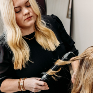 Stylist curling a client’s blonde hair in a salon