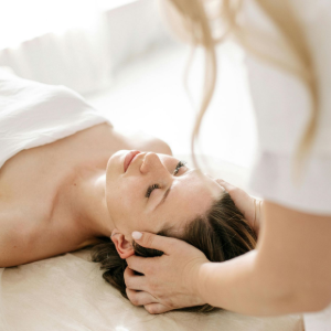 Woman receiving a head massage on a bed, eyes closed, in a bright spa-like room
