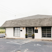 Small white storefront with large windows and parking spaces in front