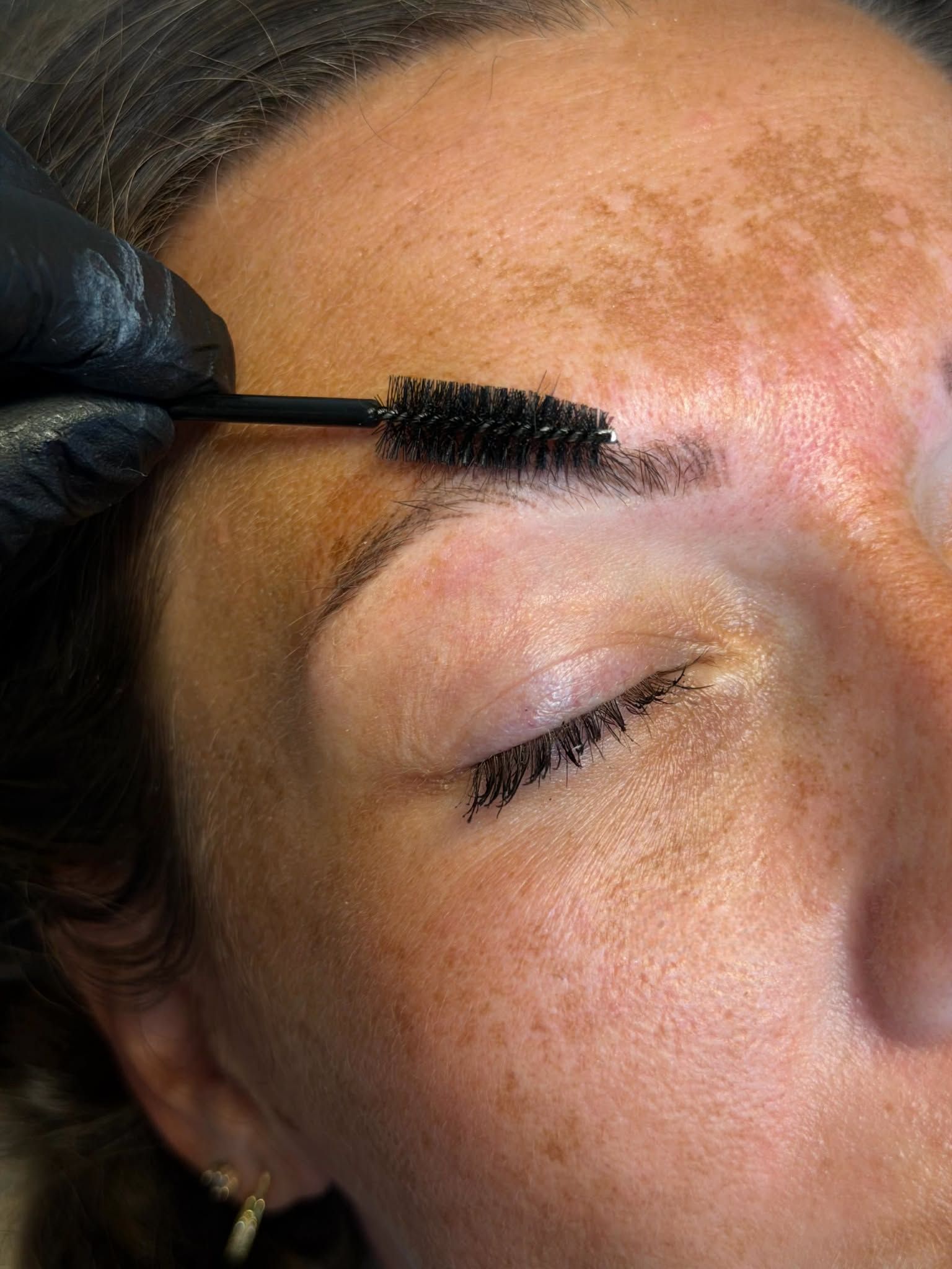 Close-up of a person’s face with an eyebrow pencil applied, looking upward indoors
