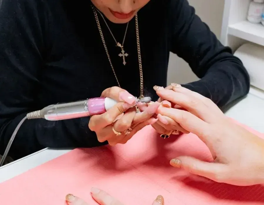Nail technician using an electric file on a client’s nails over a pink mat