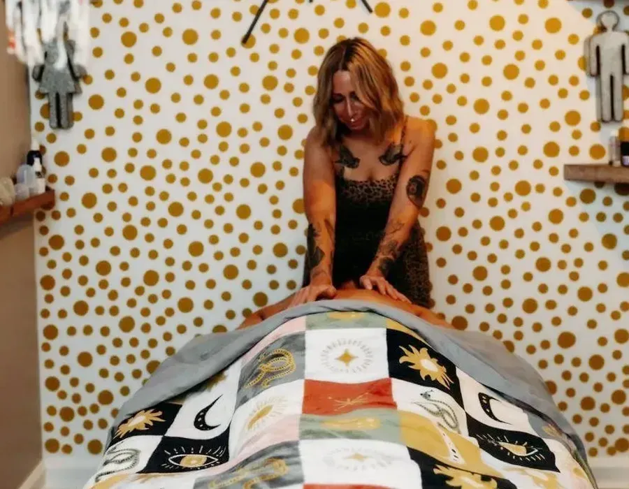 Person standing at the foot of a patchwork quilt in a polka-dot room with a sun wall decoration