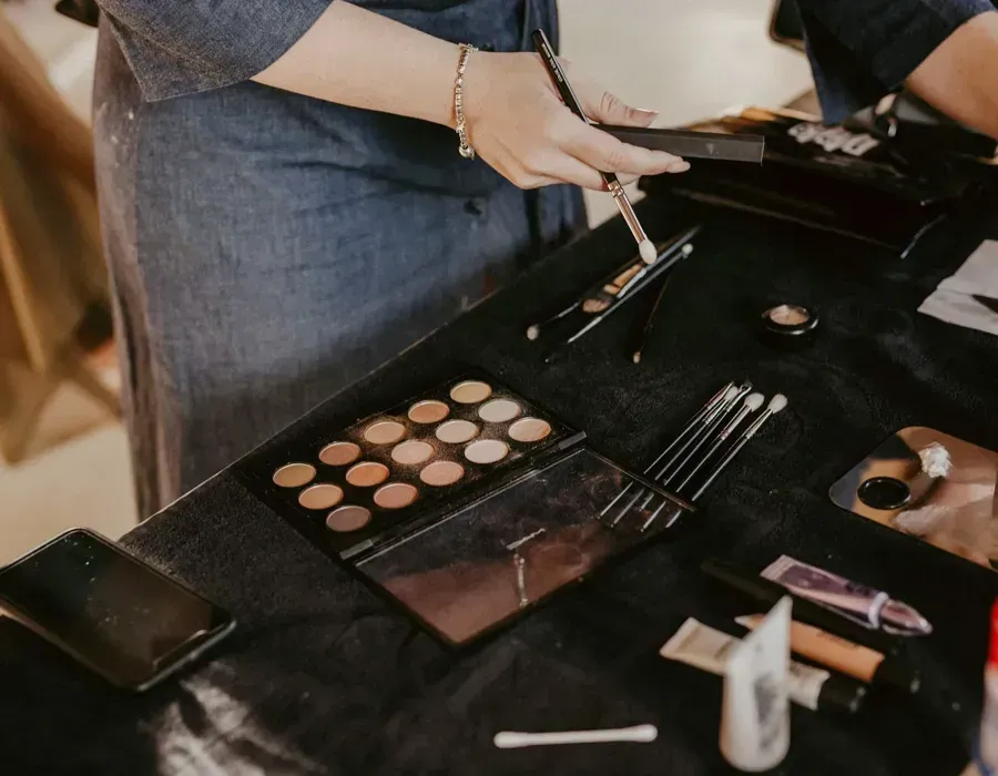 Open makeup kit with brushes and palettes on a table as a person reaches in.