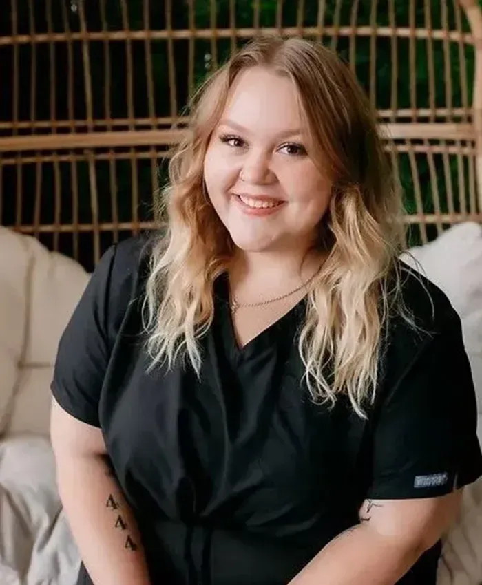 Smiling person in a black top seated indoors against a woven screen backdrop