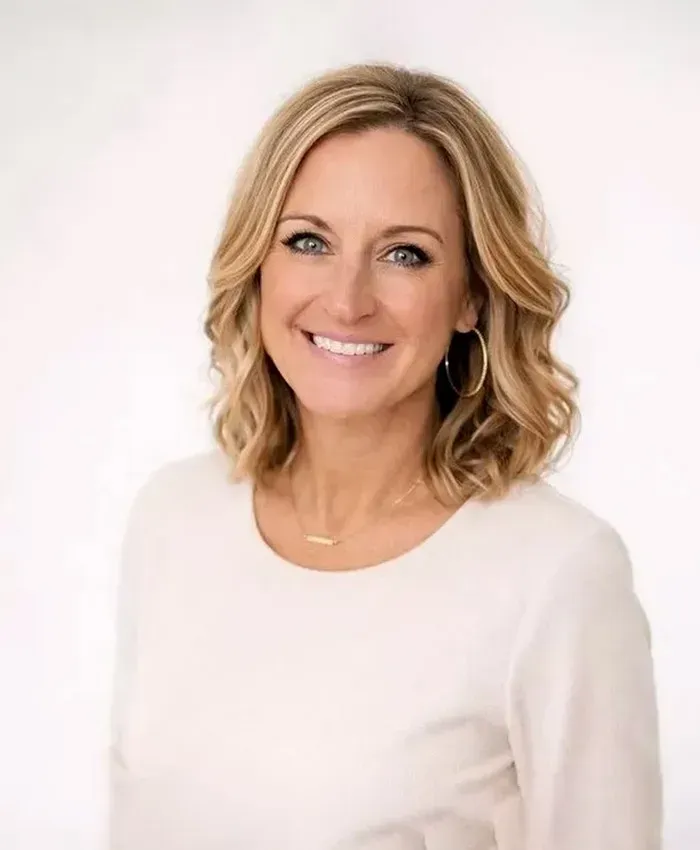 Smiling woman with shoulder-length blonde hair in a white top against a light background