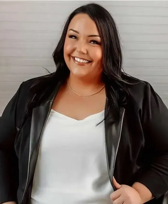 Smiling person in a black jacket over a white top against a light gray background