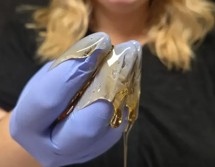 Gloved hand holding a clear jelly-like substance with a thin strand dripping downward