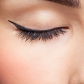Closed eye with long black eyeliner and curled eyelashes on soft skin background