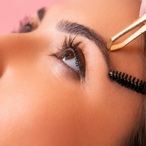 Close-up of an eye being groomed with a mascara wand and tweezers