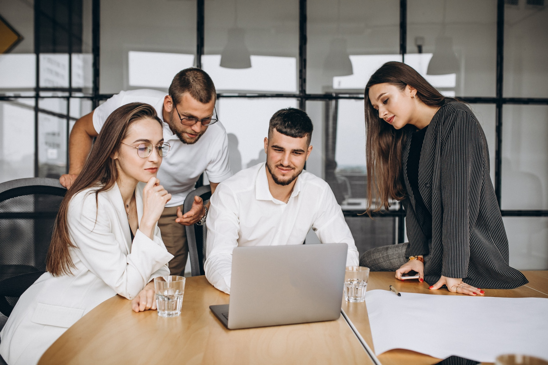 Four business people around a laptop, discussing a project in an office setting.