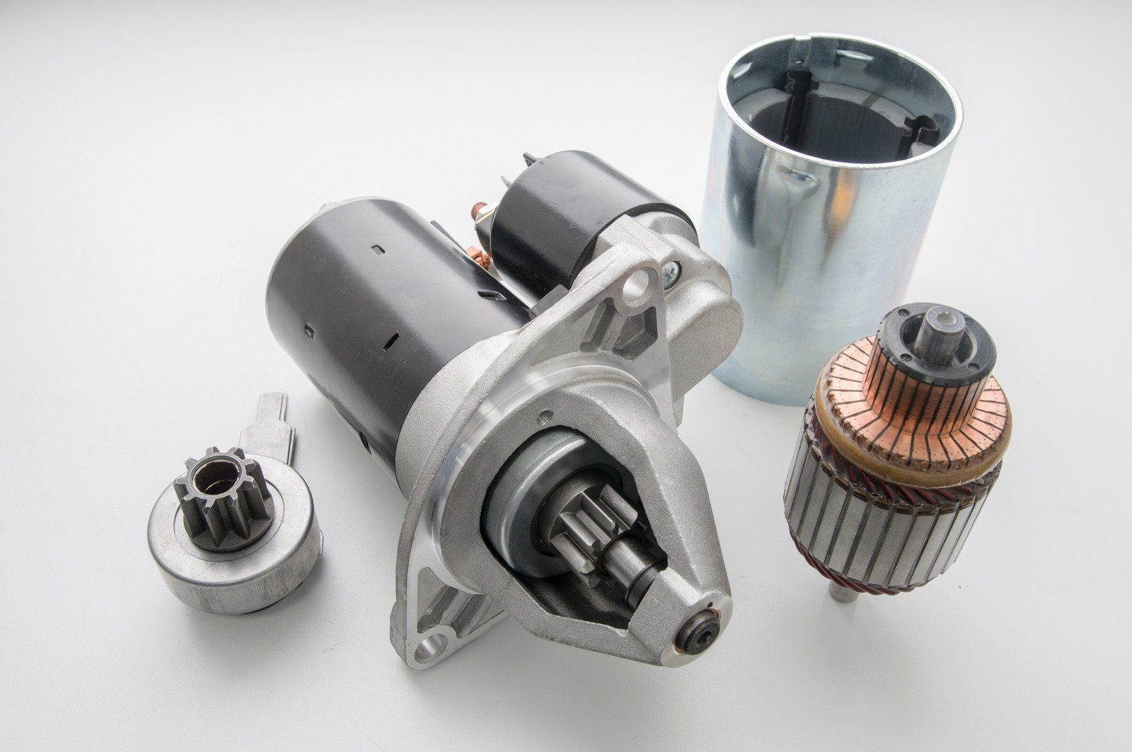 A starter motor is sitting on top of a table next to other parts.