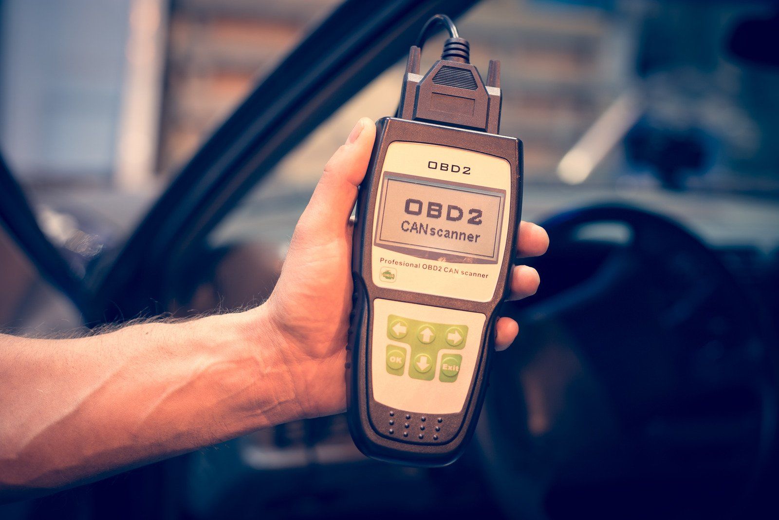 A person is holding a device in their hand in front of a car.