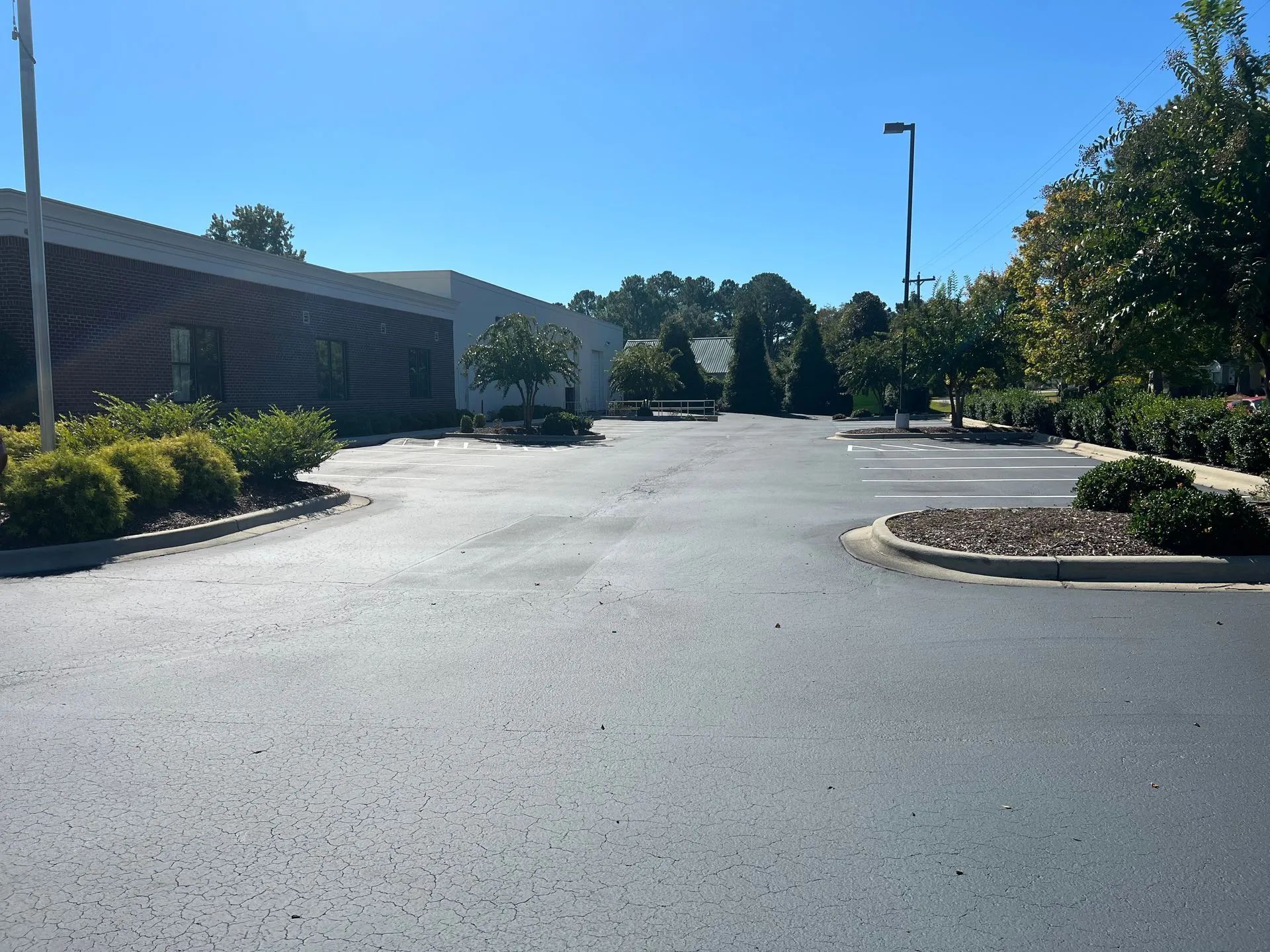 Empty parking lot beside a brick building and landscaped curbs on a sunny day
