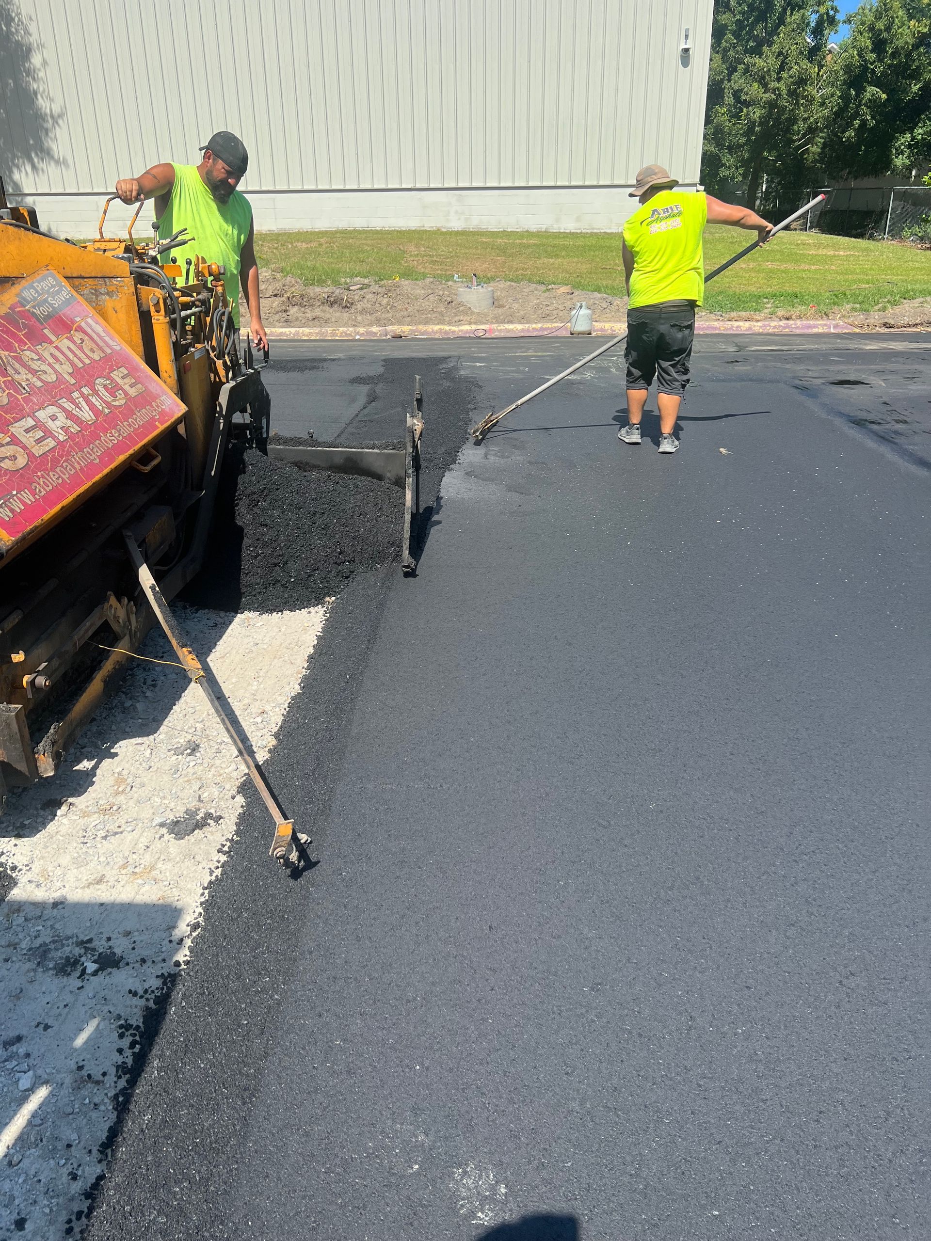Two workers paving a road with asphalt. One operates the paver, the other spreads the asphalt.