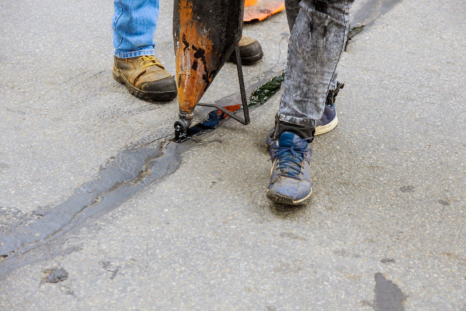 Two people sealing a crack in asphalt with gray sealant; close-up view.