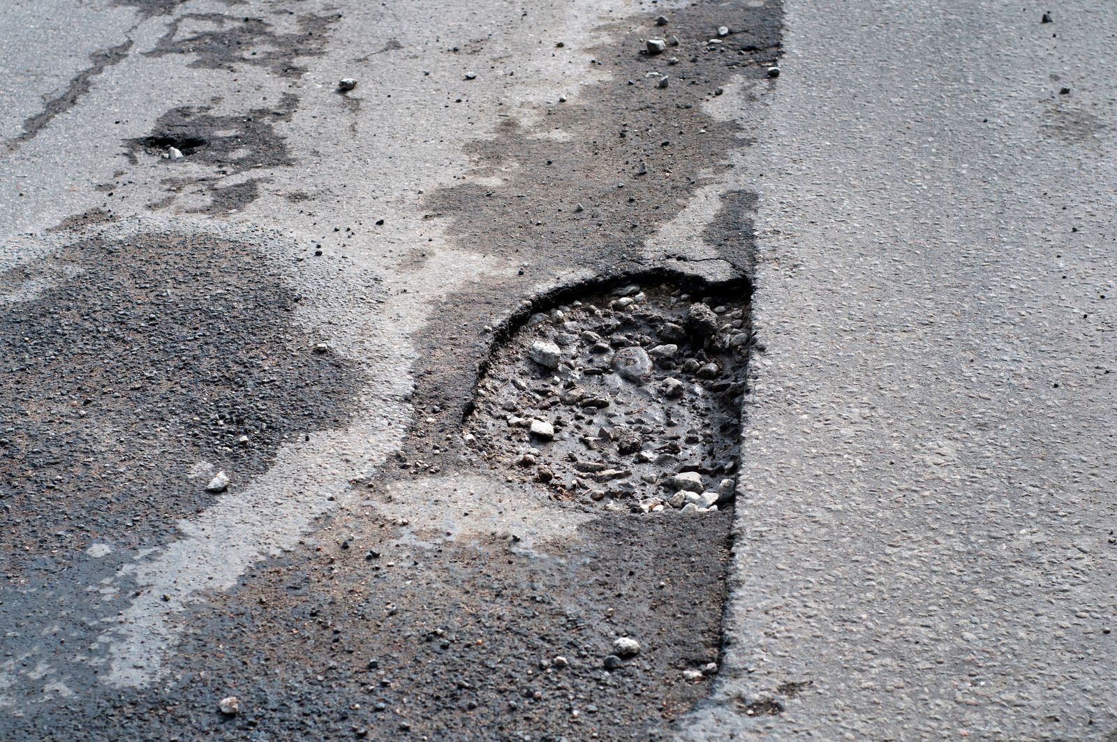 Pothole in a damaged asphalt road with rough patches and crumbling edges
