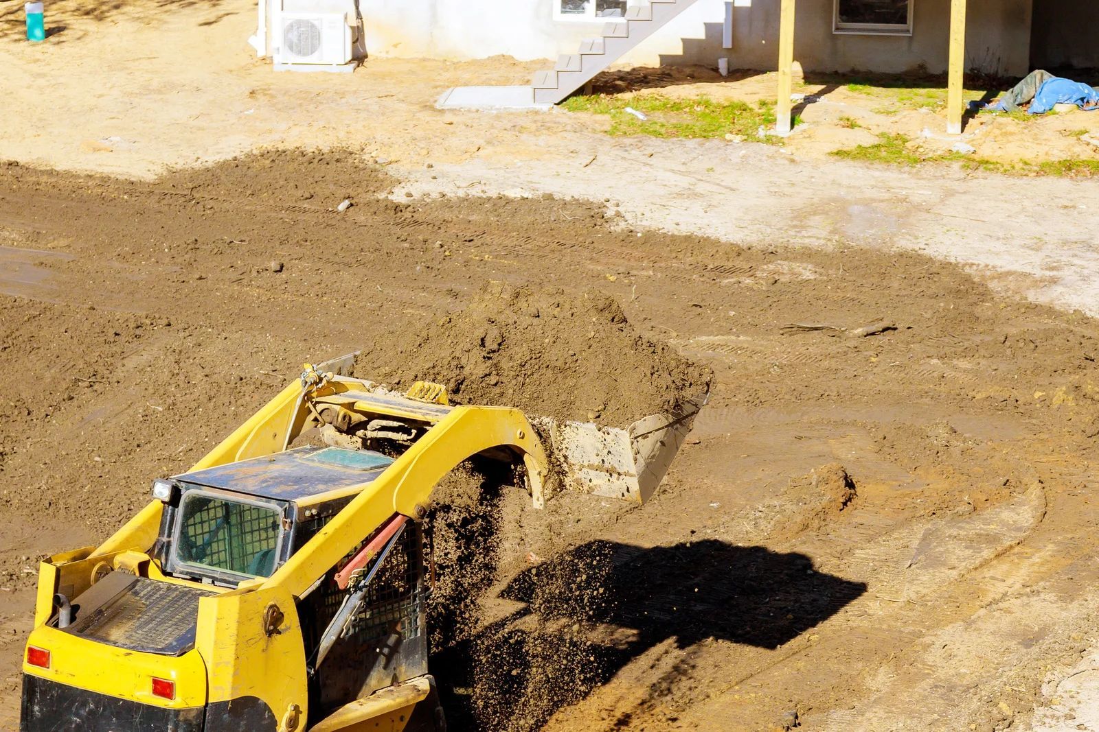 Yellow skid steer dumping dirt at a construction site