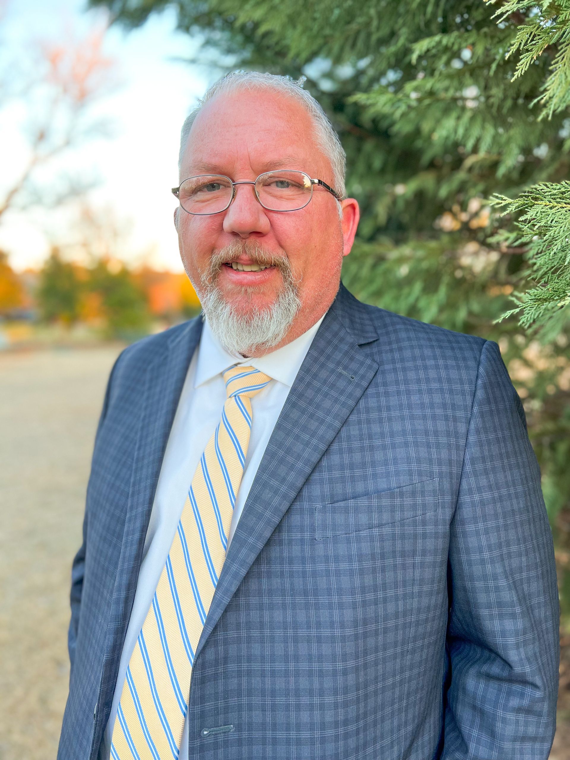 A man in a suit and tie is standing in front of a tree.