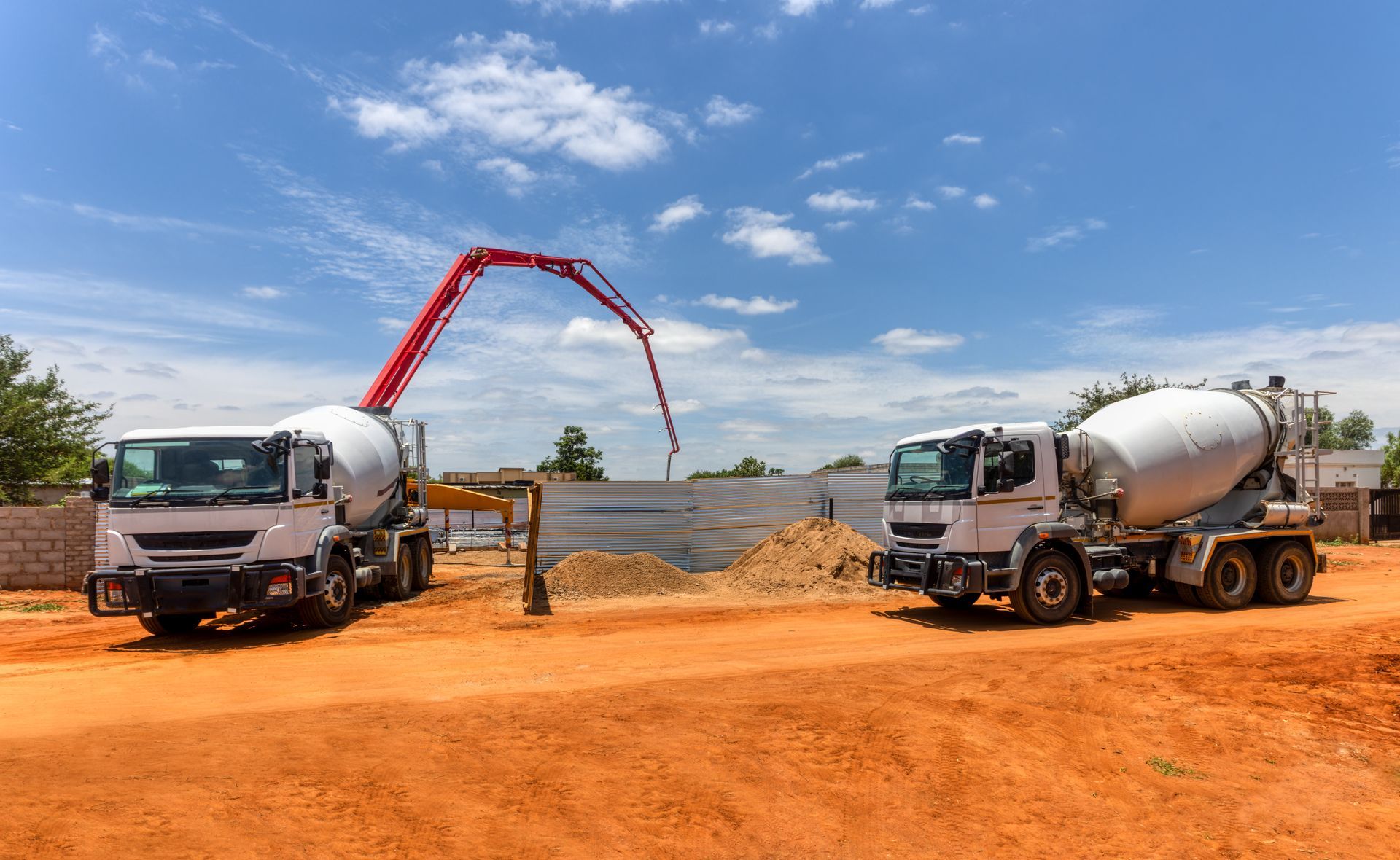 Two White Cement Trucks on a Dirt Lot With a Red Concrete Pump — Nambucca Concrete Pumping in Valla, NSW