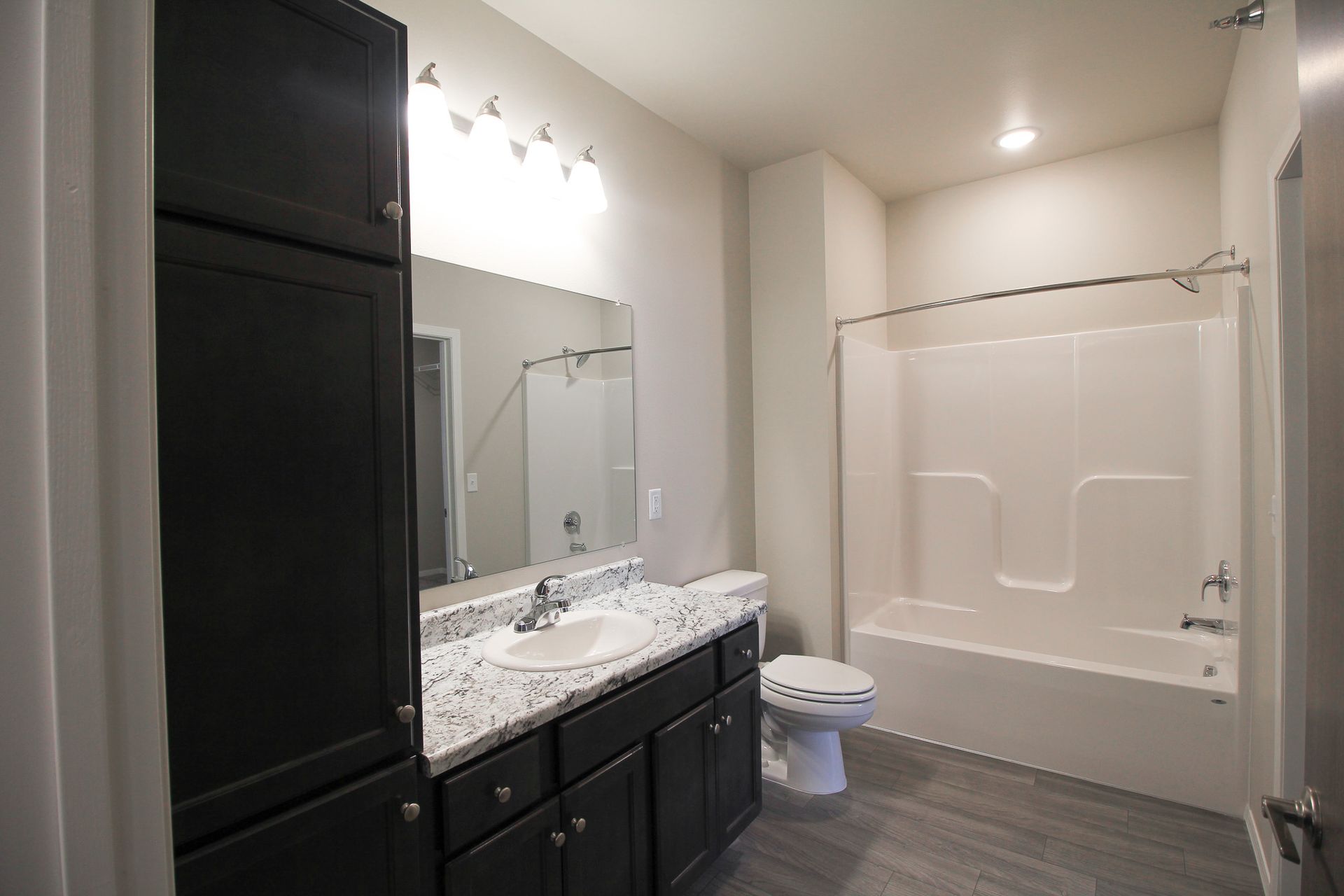 Modern bathroom with dark vanity, large mirror, tub-shower, and toilet on gray tile floor