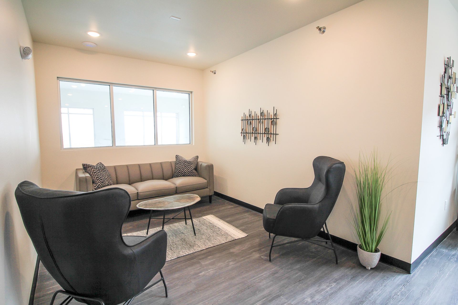 Modern waiting room with black chairs, gray sofa, rug, and wall decor under bright windows